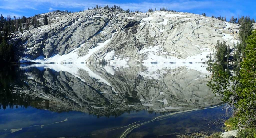 An alpine lake reflects the snow covered mountain nestled beside it. 